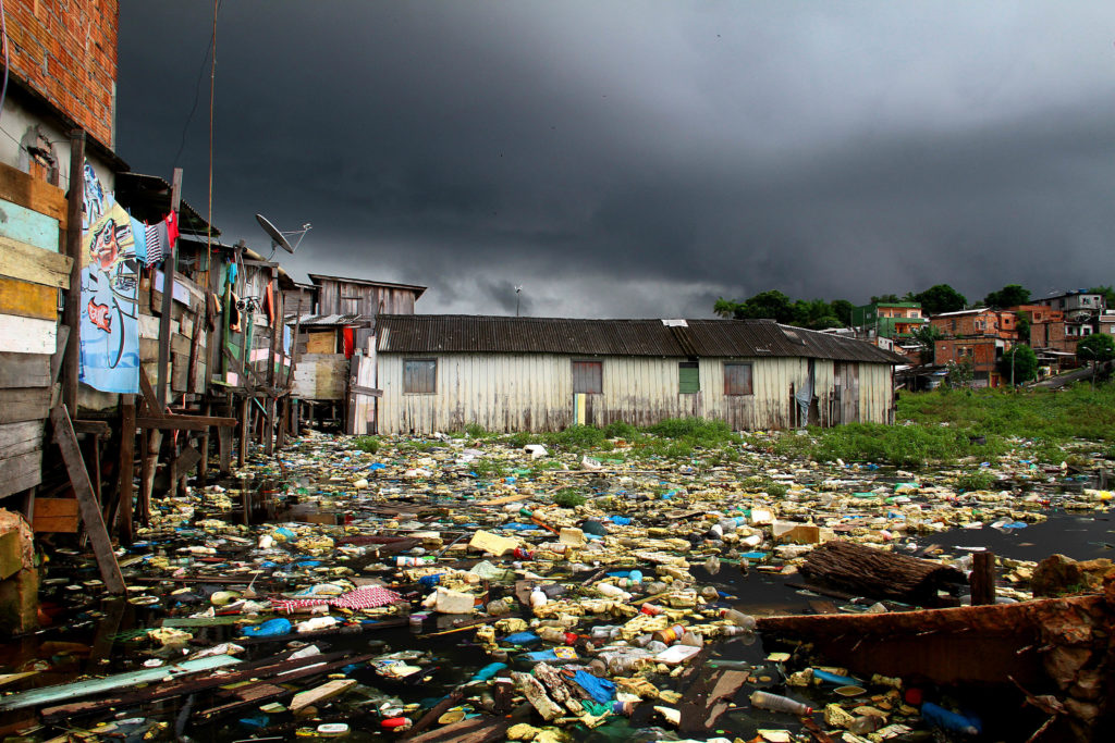 Entulho e moradias em igarapé de Manaus com céu nublado ao fundo.