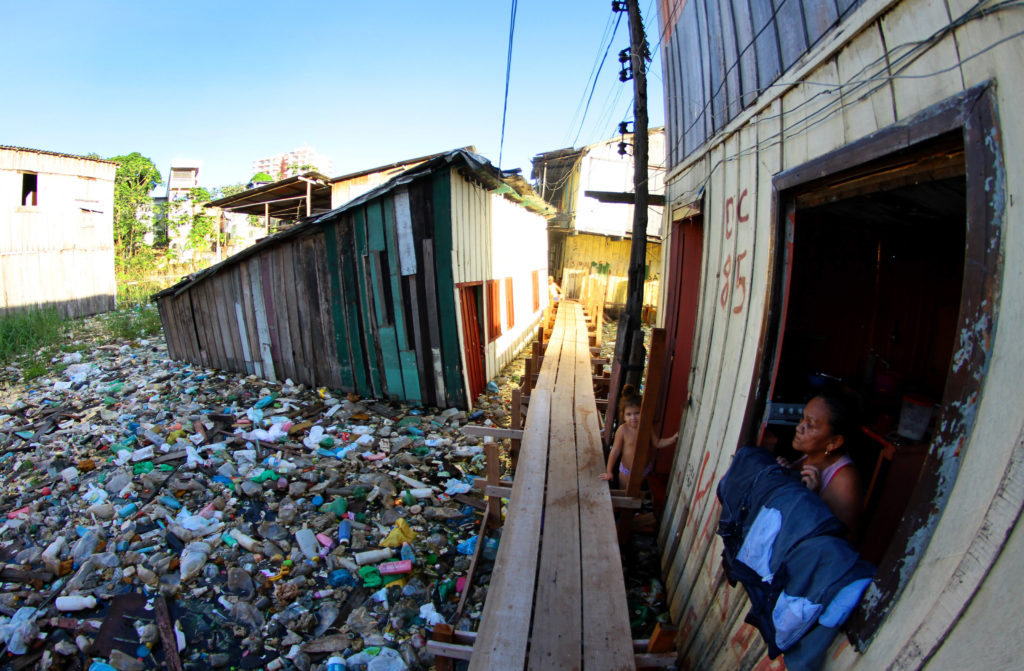 Mulher na janela e criança na passarela de madeira em meio a grande quantidade de lixo em igarapé de Manaus.