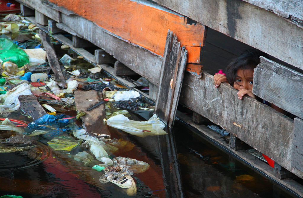 criança observa lixo pela janela de sua casa em Manaus.