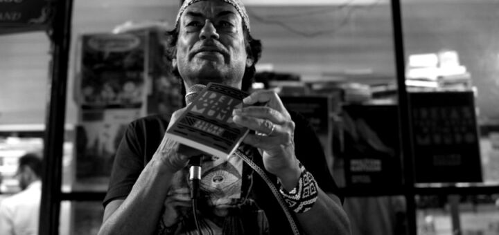 Ailton Krenak em preto e branco, segurando o livro Ideias para adiar o fim do mundo