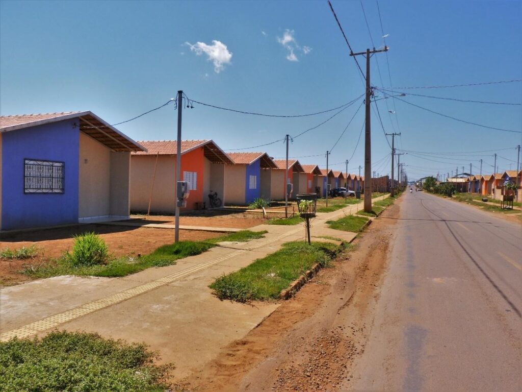 Foto de um conjunto de casas iguais roxas e laranjas. As casas se estendem por toda rua.