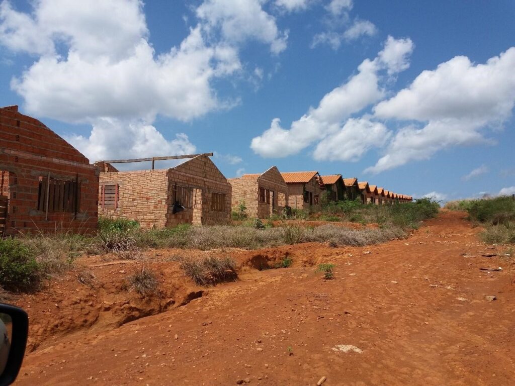Foto de casas abandonadas em uma estrada sem terra. Algumas construções não apresentam teto.