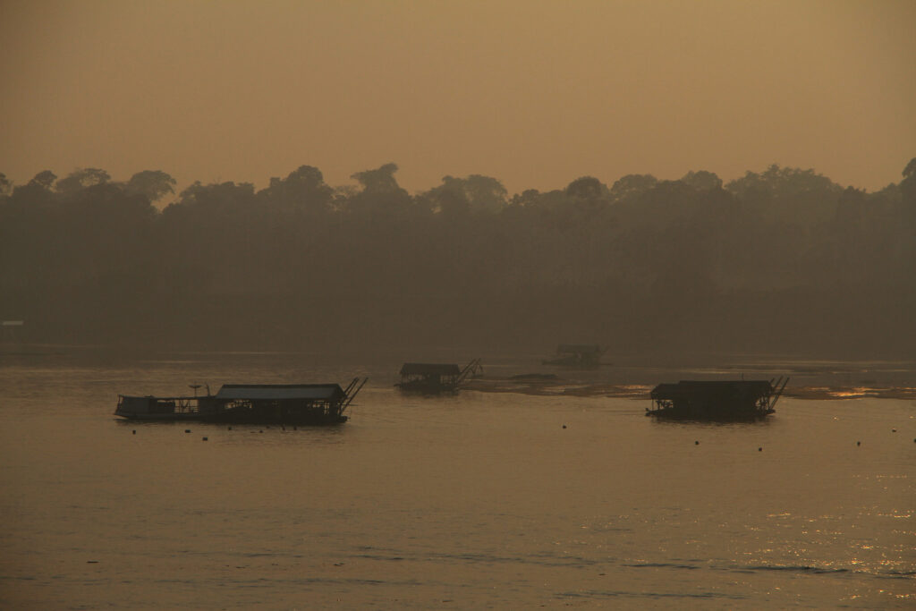 embarcações em um rio. Fumaça embaça a vista. O fundo está amarelado pelo incêndio