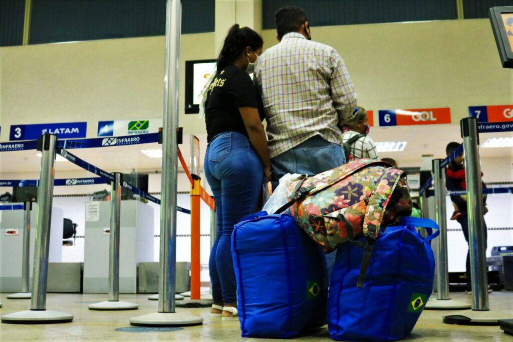 Uma mulher encosta a cabeça no ombro de um homem na fila de espera em um aeroporto.