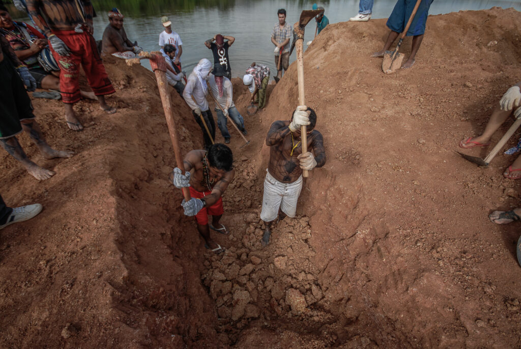 Um grupo de indígenas usa enxadas na beira de um rio