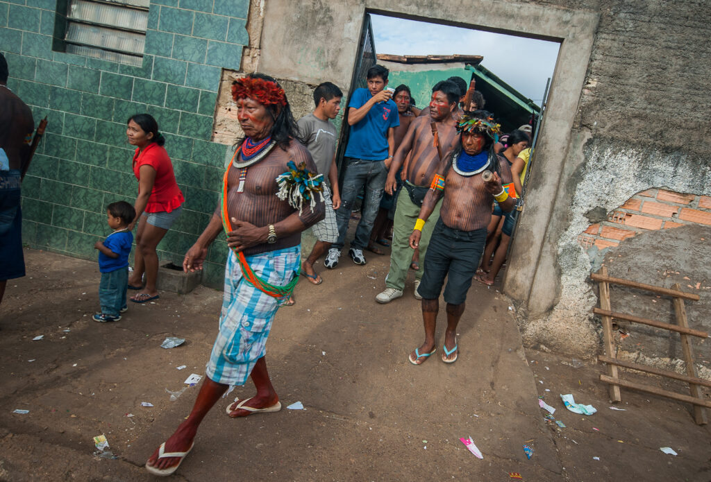 Grupo de indígenas em uma construção. Eles vestem cocar e outros apetrechos