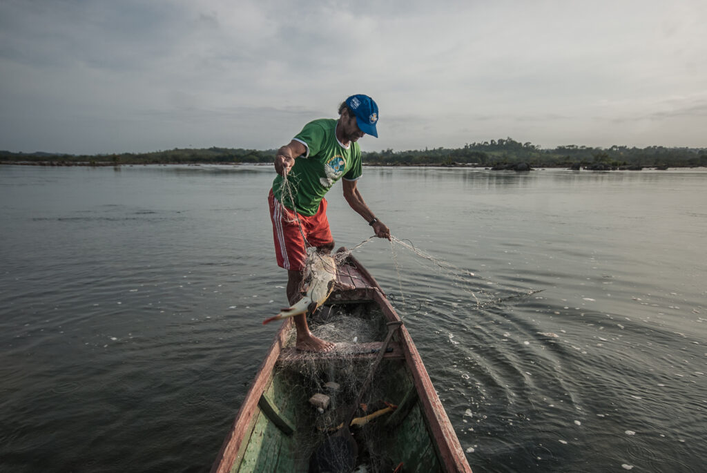 Um homem segura um peixe em uma rede, de pé em uma canoa.