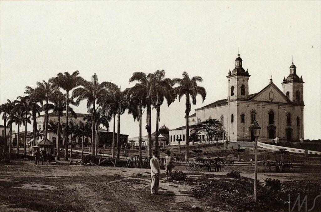 Foto em preto e branco de uma Igreja no horizonte, cercada por palmeiras.