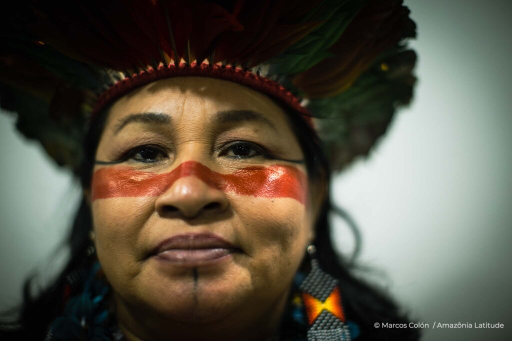 Telma vestindo um cocar e pintura facial vermelha