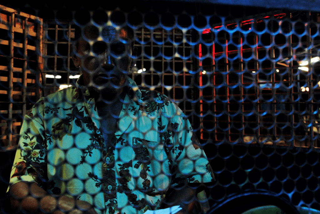 Um homem de pé, atrás de uma cerca de metal sob luz azul