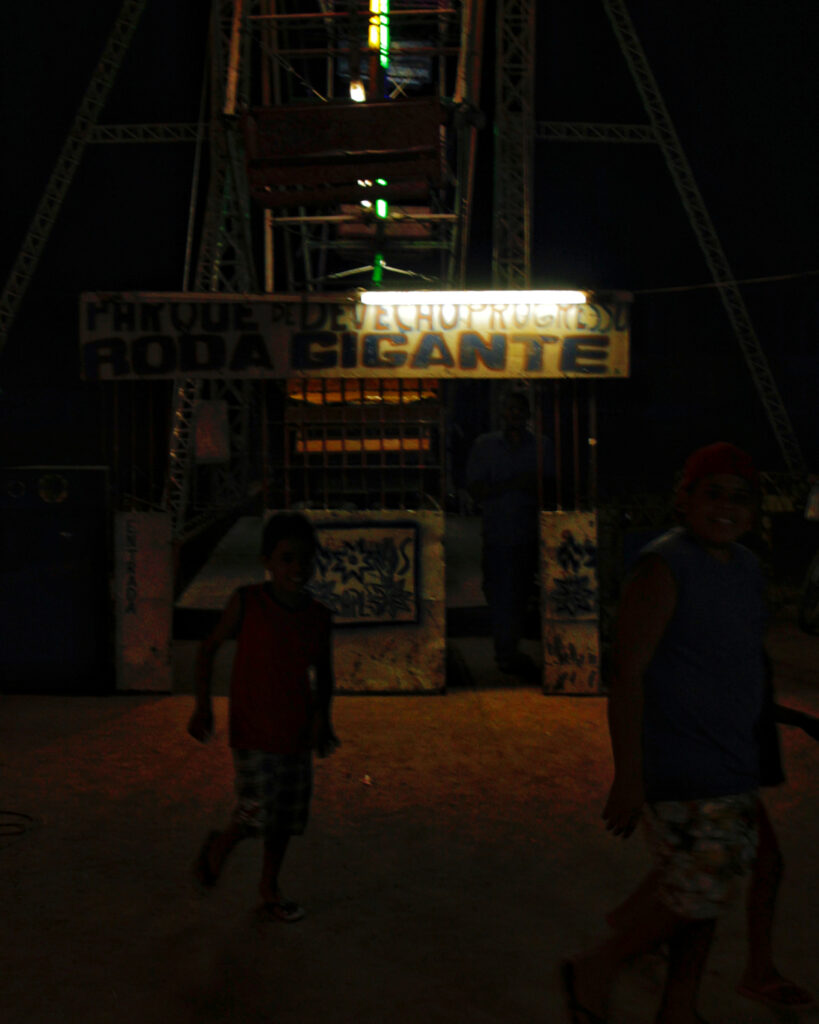 Crianças correm em um local pouco iluminado próximo à roda gigante do Parque Progresso