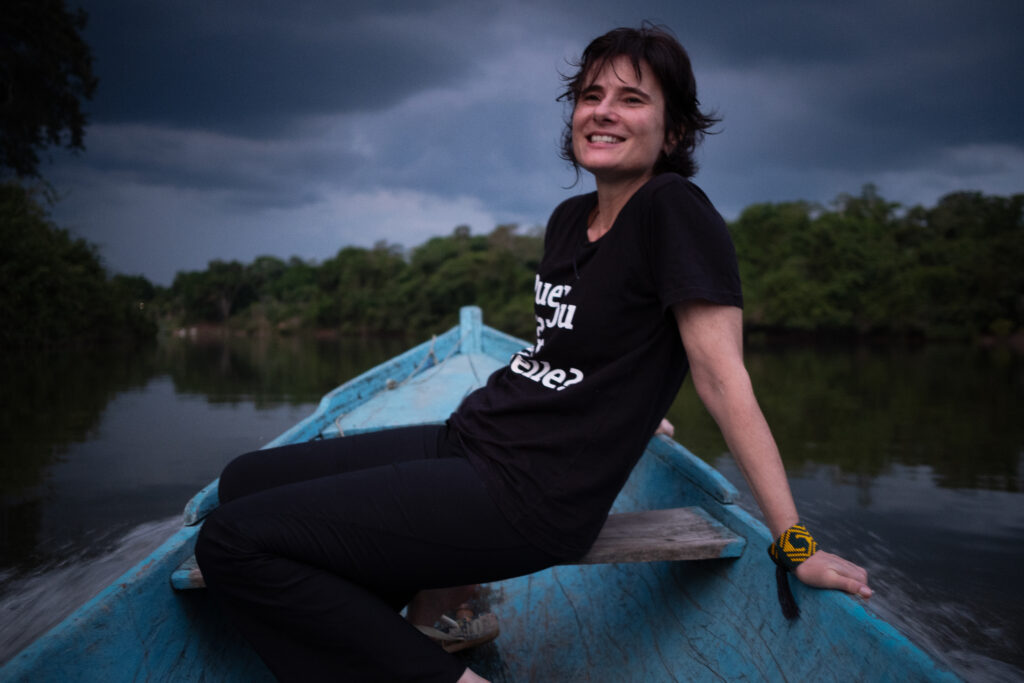 Eliane Brum, sentada em um barco azul. Imagem do livro Banzeiro Òkòtó