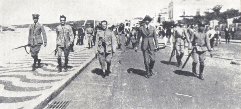 Foto antiga em preto e branco, levemente granulada, de oficiais da marinha andando pelo calçadão de Copacabana, no Rio de Janeiro, no que foi a Revolta dos 18 do Forte.