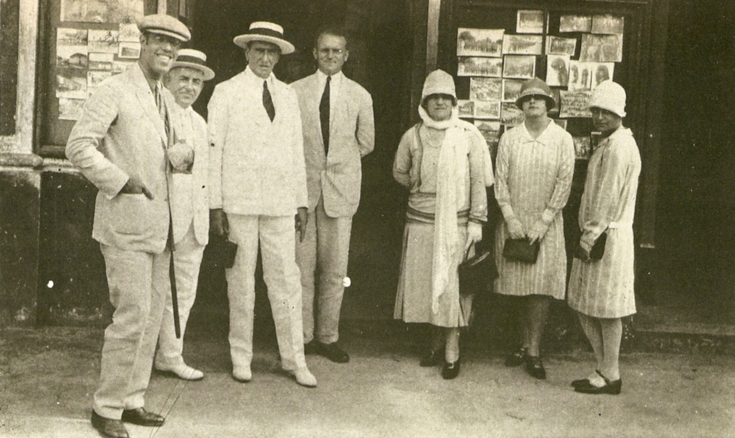 Foto antiga em sépia de Mário de Andrade, à esquerda, ao lado de seis pessoas não identificadas. Os quatro homens, todos à esquerda, usam terno e gravata e apenas um não usa chapéu. As três mulheres, à direita, usam vestidos até as canelas, carregam bolsas pequena e usam chapéu tipo clochê.