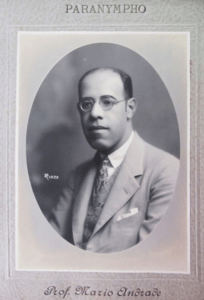 Retrato do poeta Mário de Andrade, em preto e branco. Mário é um homem branco, levemente calvo, eusa um terno e óculos de armação redonda.