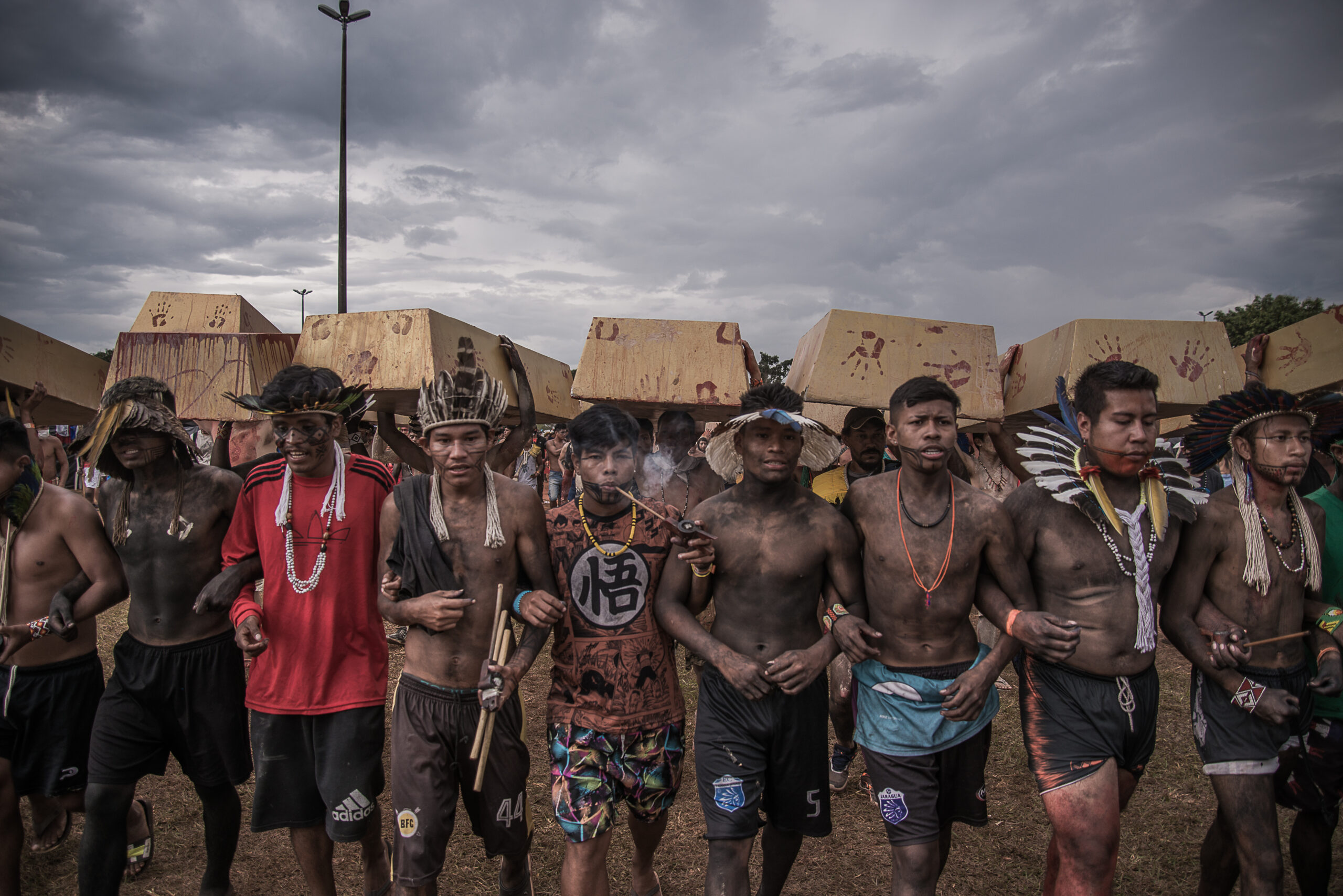 Indígenas protestam contra o garimpo ilegal na Amazônia no Acampamento Terra Livre, segurando caixões nas costas durante uma marcha.