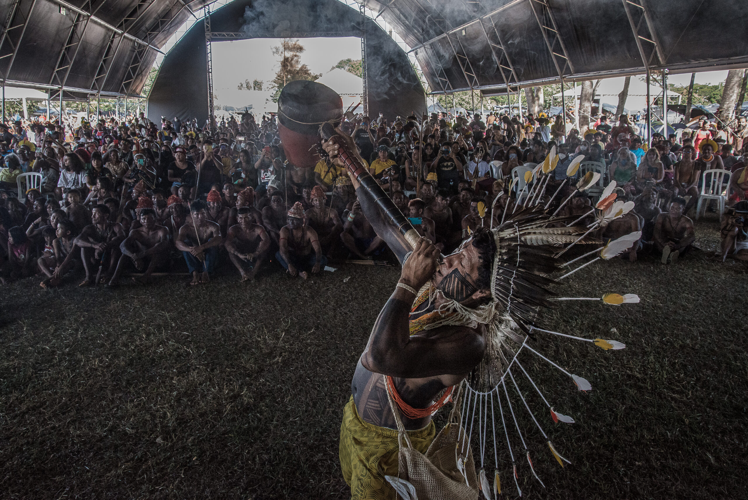 Homem indígena toca instrumento em frente a manifestantes do Acampamento Terra Livre