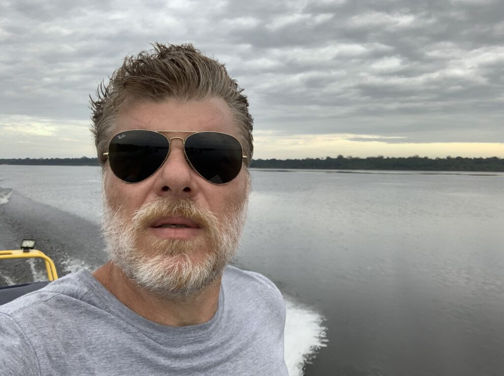 Flávio Cremonesi. Um homem de barba branca, óculos escuros, num barco.