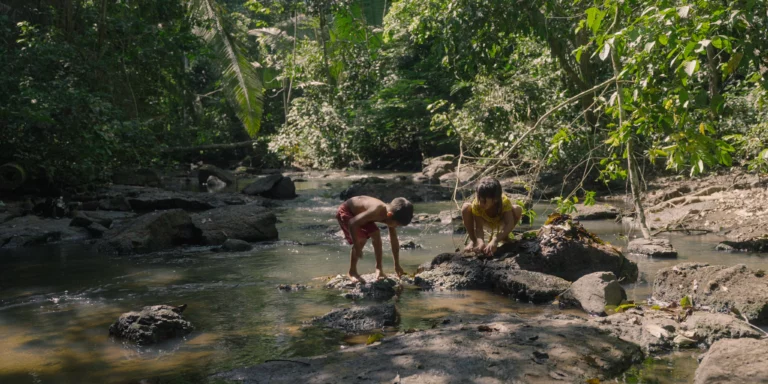 Garoto e garota indígenas brincando em um riacho.