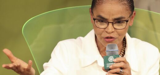 Marina Silva, de terninho branco, coque alto e óculos, discursa em microfone.