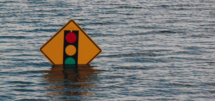 Placa de trânsito com a imagem de um semáforo quase totalmente submersa em uma enchente