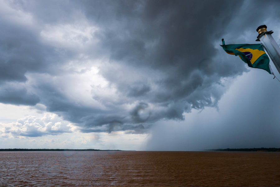 Chuva caindo sobre a Amazônia, com bandeira do Brasil em frente.
