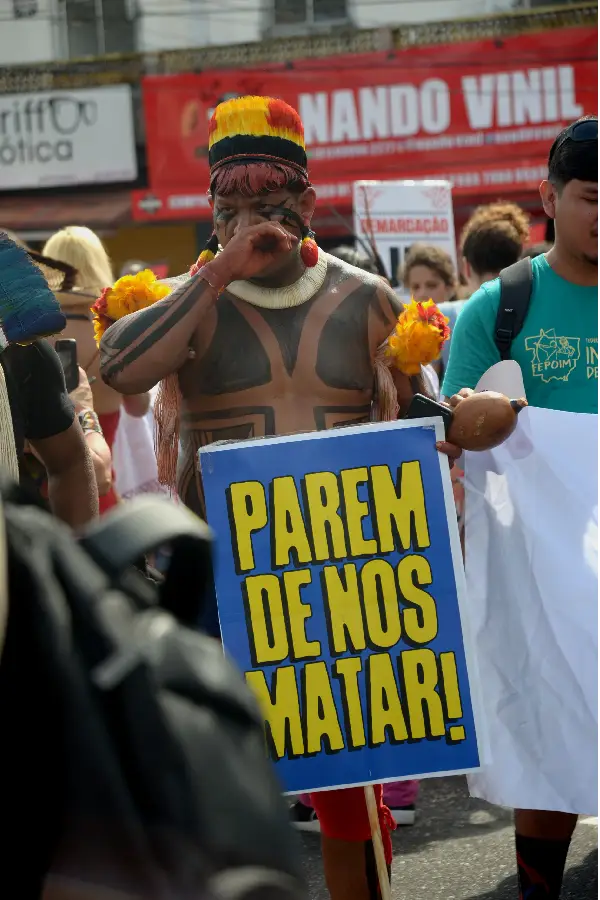 O Grito Pela Vida: Em um dos momentos mais contundentes da Marcha, um guerreiro indígena ergue a faixa que confronta diretamente a violência no campo e a invisibilidade nos debates da COP30: "Parem de nos Matar!". Foto: Isabela Leite/Amazônia Latitude.