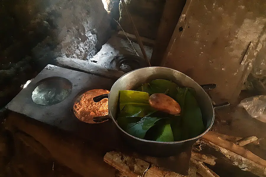 O Nozãkubu (bolo de milho) sendo cozido no fogão a lenha. A panela, revestida pelas folhas criteriosamente escolhidas, garante o cozimento e o sabor tradicional deste alimento. Foto: Luana Oliveira.