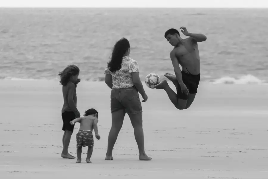 O movimento e a descontração ganham a faixa de areia na Ilha de Maiandeua. Jovem se projeta no ar durante um jogo de futebol à beira-mar, emoldurado pelo olhar atento das crianças e pela imensidão do horizonte atlântico. Foto: Oswaldo Forte/Amazônia Latitude.