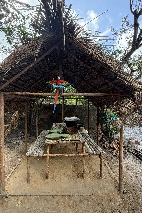 Mesa e bancos confeccionados com varas nativas sob a cobertura de palha: espaço de comensalidade e partilha no Quintal Ancestral, decorado com artefatos de fibra trançada e artesanato local. Foto: Miguel Picanço/Amazônia Latitude.