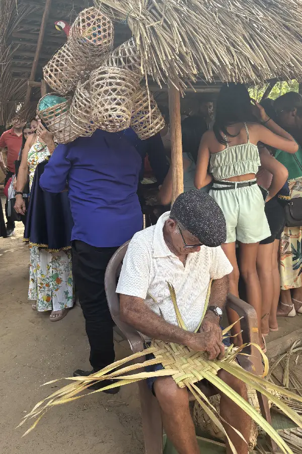 Artesão local trança palha nativa sob o olhar de visitantes e moradores, transmitindo técnicas tradicionais de confecção de artefatos utilitários em Araí. Foto: Miguel Picanço/Amazônia Latitude.