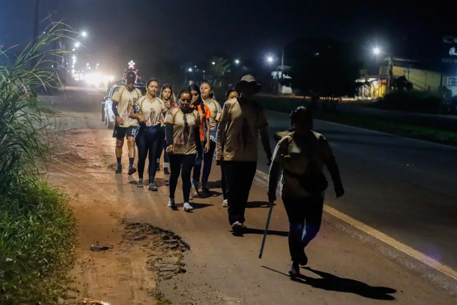 Na penumbra da madrugada, um grupo de romeiros caminha em fila pelo acostamento, com os passos iluminados apenas pelos faróis distantes e pela fé que os guia na longa jornada para Ananindeua. Foto: Oswaldo Forte/Amazônia Latitude.